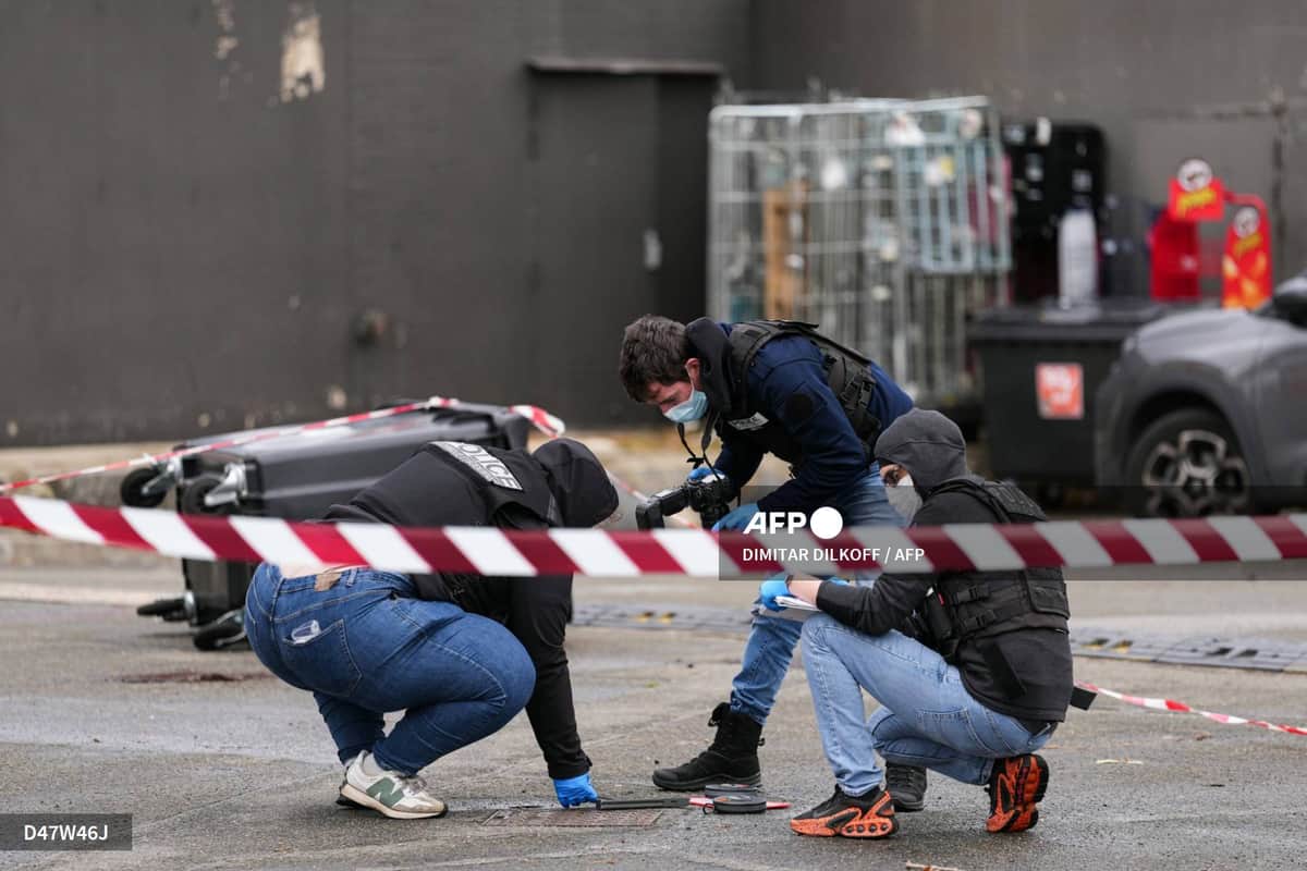 Trois enquêteurs de la police accroupis derrière un ruban de sécurité, examinant le sol