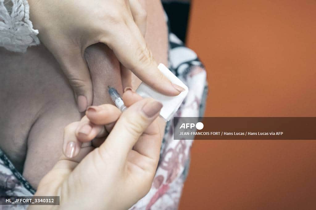 Une soignante pique le haut du bras d'une femme âgée avec une seringue, en tenant la peau avec une compresse