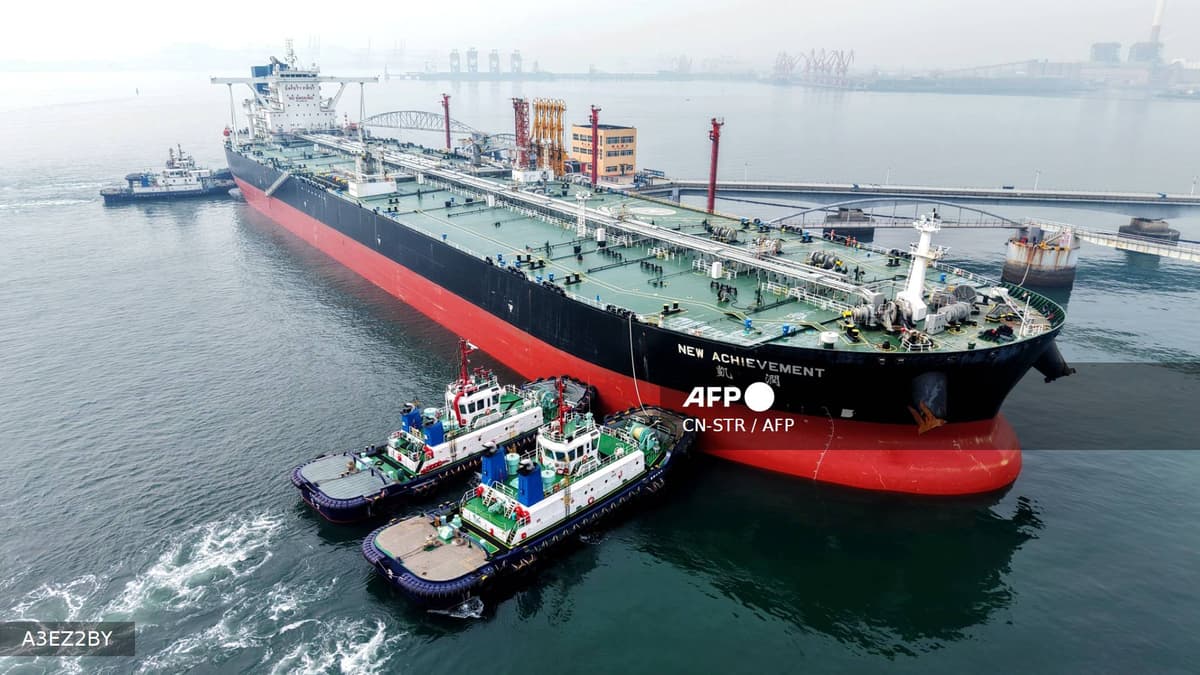 Vue aérienne d'un pétrolier géant amarré à un terminal portuaire, entouré de remorqueurs